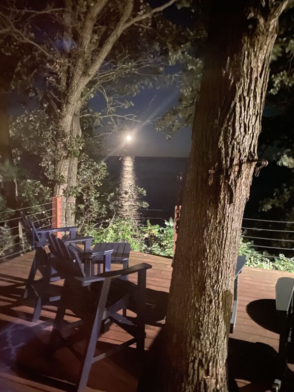 An outdoor deck with chairs and a table, surrounded by trees, overlooking a body of water.