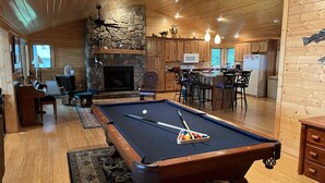 Interior acogedor de una cabaña con mesa de billar, piano, chimenea y comedor de madera.