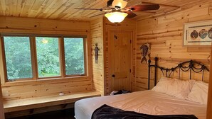 Un dormitorio de cabaña de madera con una cama, una ventana, un ventilador de techo y una puerta.