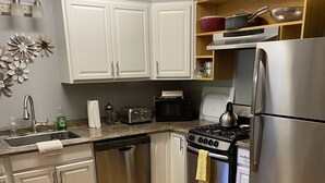 A compact kitchen with white cabinets, a stainless steel refrigerator, a stove, and a microwave.