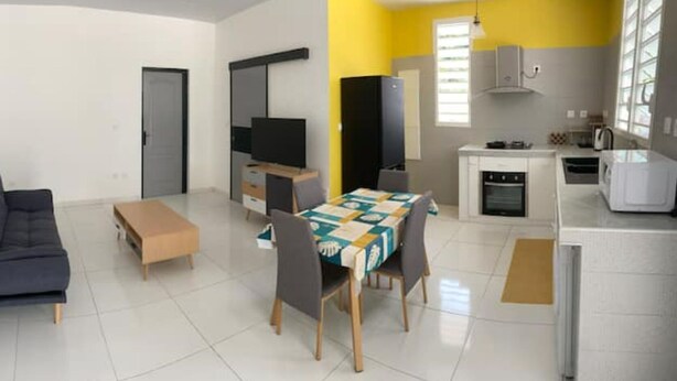 Un espace de vie moderne comprenant un canapé, une petite table, une table à manger avec des chaises, un coin cuisine avec un four à micro-ondes et un téléviseur.