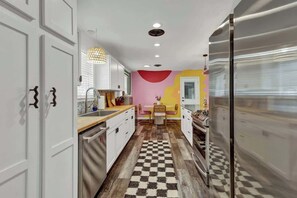 A narrow kitchen with white cabinets, a checkered floor, a pink wall, and a modern refrigerator.