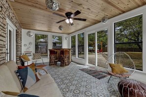 A spacious room with a wooden ceiling, large windows, a ceiling fan, and a dining area with a table and chairs. - Blue Succulent Haus: Hot-Tub 4 Min to Downtown! (Fredericksburg)
