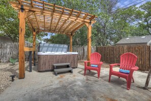 A wooden pergola with a hot tub and two Adirondack chairs in a backyard.