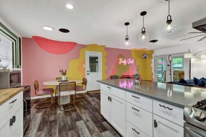 A modern kitchen with a central island, white cabinetry, and a colorful abstract wall design. - Blue Succulent Haus: Hot-Tub 4 Min to Downtown! (Fredericksburg)
