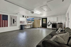 Ein geräumiger Raum mit grauem Teppich, einer grauen Couch mit gestreiftem Kissen und einer schwarzen Tür, einem weißen Schrank und einem an der Wand montierten Fernseher.