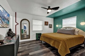 A bedroom with a bed, a ceiling fan, a large mirror, and a TV on the wall.