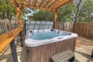 Ein Whirlpool unter einer Holzpergola mit einer hölzernen Bank daneben.