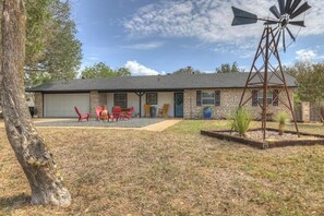 A two-story house with a garage, a windmill, and a patio with red chairs. - Blue Succulent Haus: Hot-Tub 4 Min to Downtown! (Fredericksburg)
