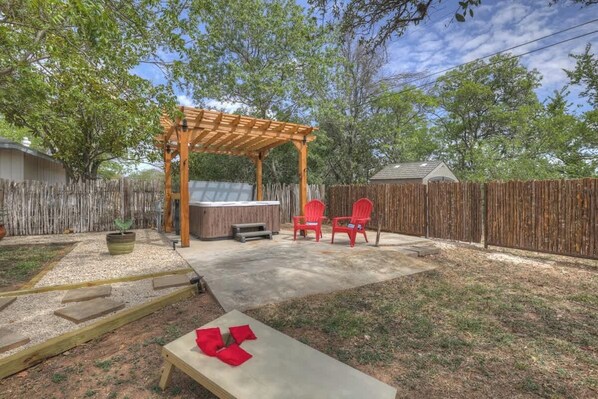 A backyard with a wooden pergola, a hot tub, and red chairs.