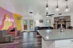 A modern living room with a large island, a fireplace, and a neon sign on the wall.