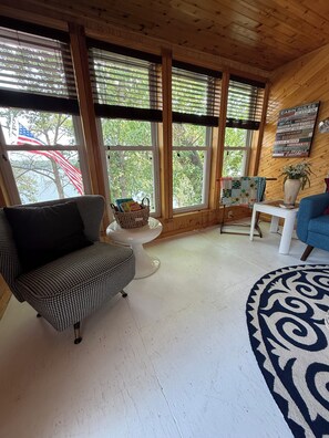A cabin interior with a houndstooth sofa, a white coffee table, a blue armchair, and a large window with blinds. - Adorable and bright lake house! Retro feel all the modern amenities (Frazee)