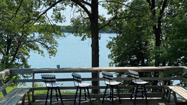 Una terraza de madera con sillas y un banco con vista a un lago.