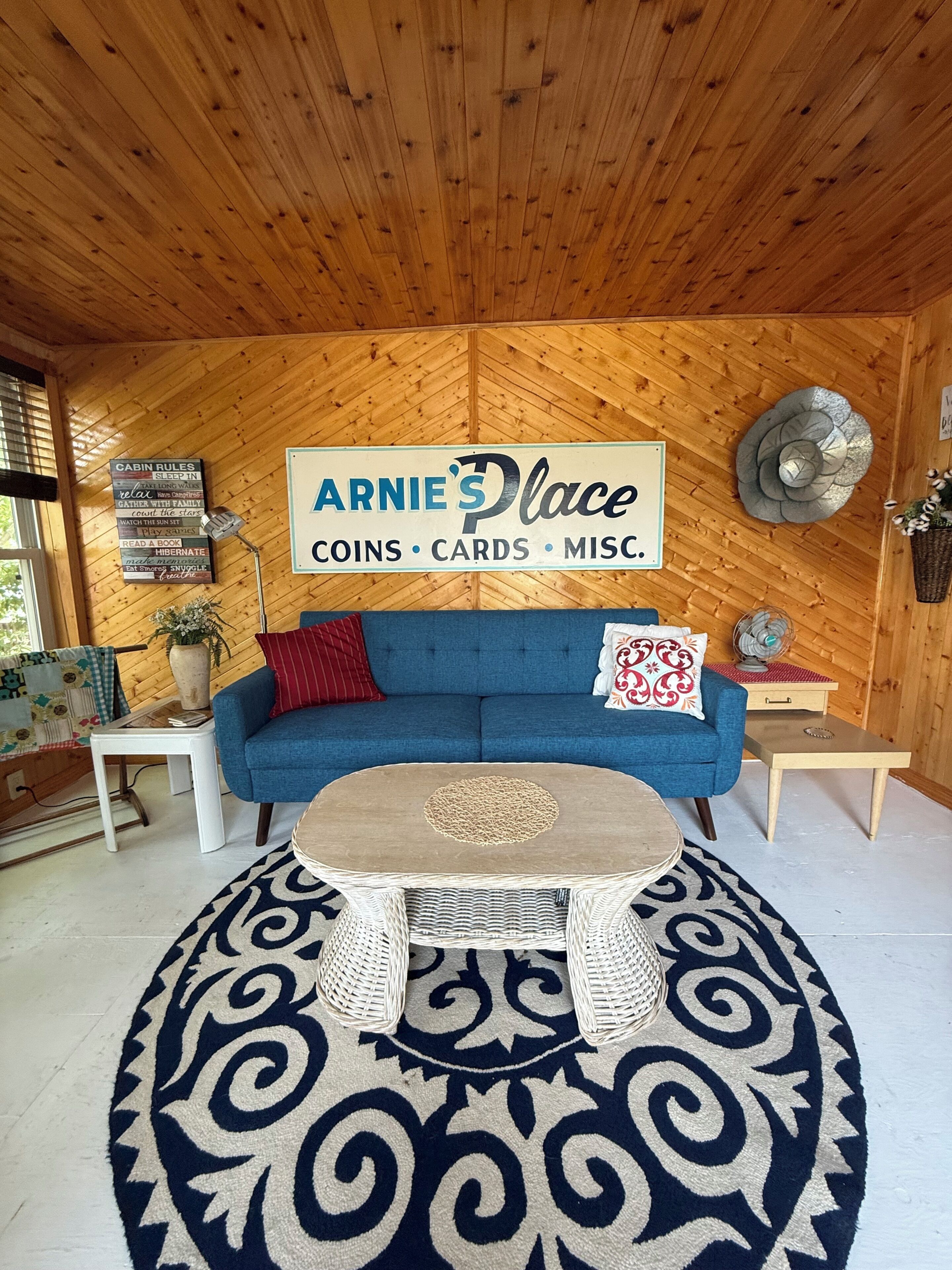 A cozy cabin interior with a blue sofa, a sign reading 'ARNIE'S Place,' and a wooden ceiling.