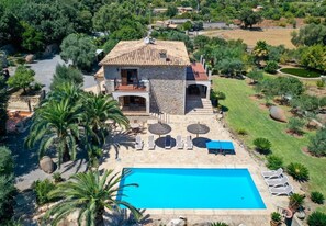 A villa with a swimming pool, sun loungers, and a garden with palm trees.