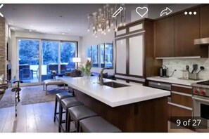 Enjoy cooking in this well-lit kitchen with a large island, sink, and oven, offering a view of the outdoors through large windows.