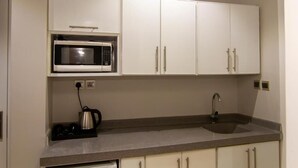 A compact kitchen with white cabinets, a built-in microwave, a kettle, and a sink. - XYZ Hotel Al Falah (Riyadh)