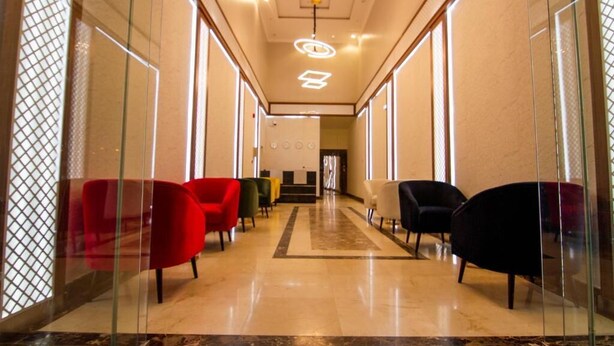 A hallway with a glass partition, red and black chairs, and a marble floor. - XYZ Hotel Al Falah (Riyadh)