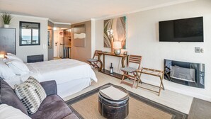 Een hotelkamer met een bed, een slaapbank, een eettafel met stoelen, een aan de muur bevestigde televisie en een open haard.