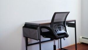 A modern office chair with a mesh backrest and armrests, positioned on a wooden desk with a drawer.