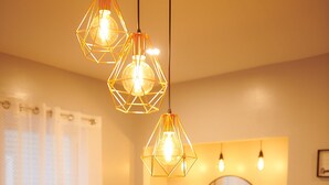 A dining area with a wooden table, a vase, and hanging geometric pendant lights.