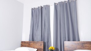 A room with two beds, grey curtains, a small table with a vase of flowers, and a wooden headboard.