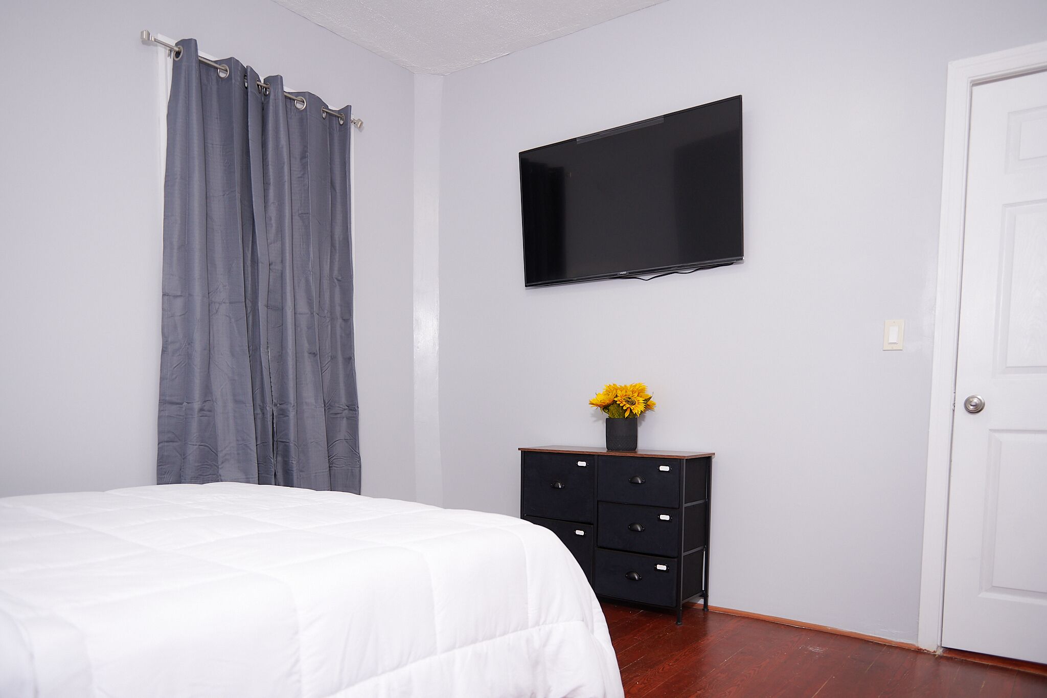Un dormitorio con una cama, un aparador, un televisor de pantalla plana y una puerta.