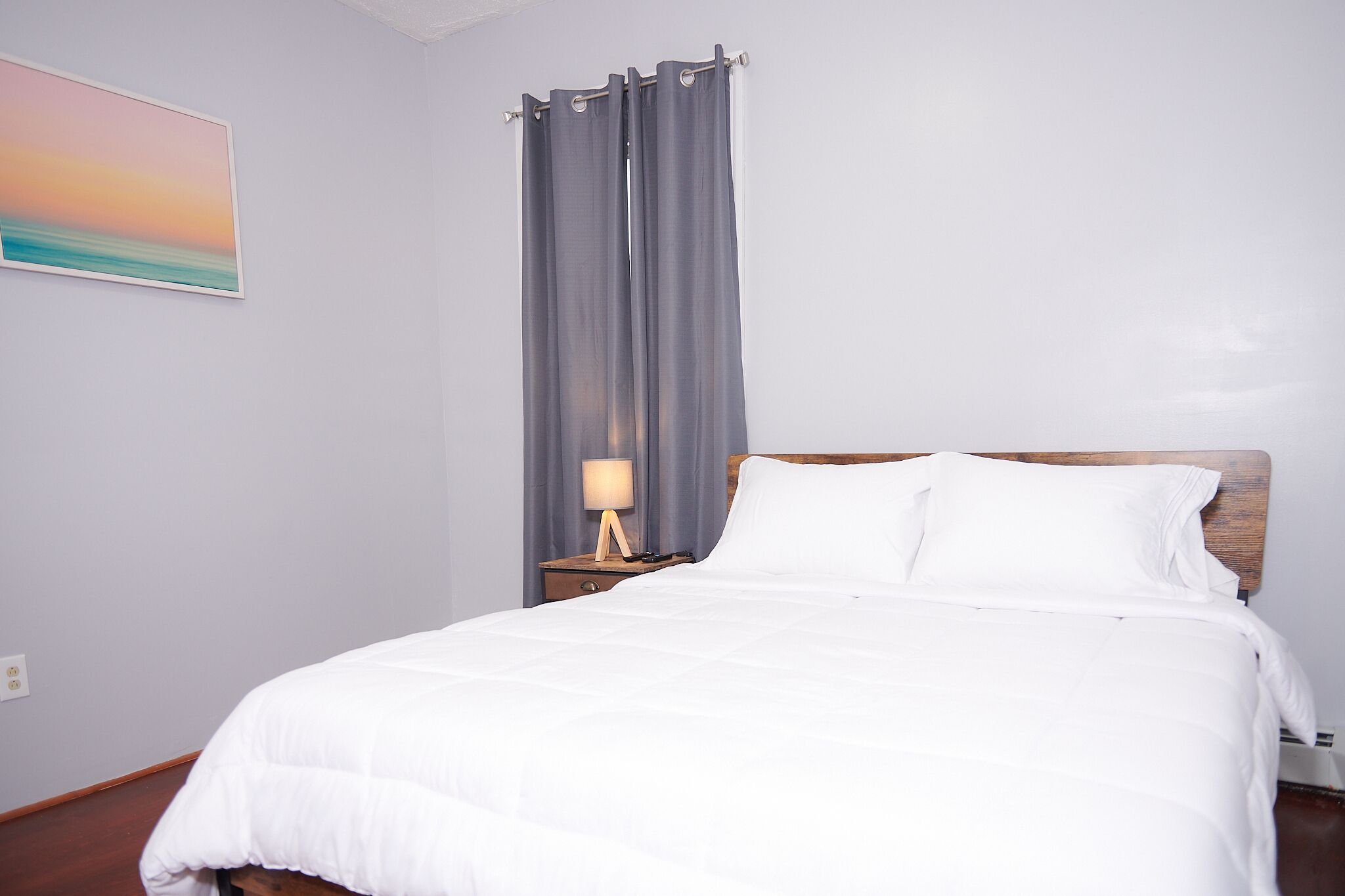Cama bem arrumada com roupa de cama branca, cabeceira de madeira e mesa de cabeceira com abajur.