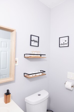 A bathroom with a white toilet, wooden shelves, and two framed signs on the wall. - Cozy apartment 2nd 10min Walk Downtown | City View (Providence)