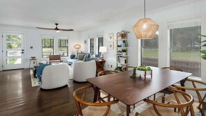 A spacious living room with a wooden dining table, white sofas, and a ceiling fan. - Pet-friendly, Hot tub, Close to Main St! (Fredericksburg)