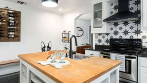 A modern kitchen with a wooden island, stainless steel appliances, and a star-patterned backsplash. - Pet-friendly, Hot tub, Close to Main St! (Fredericksburg)