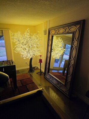 Una habitación con un espejo grande, un árbol decorativo y una mesa de fútbol de mesa.