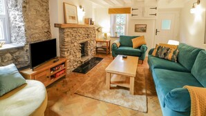 A cozy living room with a stone fireplace, a television, a green sofa, and a wooden coffee table. - Carreg Winllan (Pen-y-sarn)