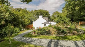 A white house with a gravel driveway, surrounded by lush greenery and trees. - Carreg Winllan (Pen-y-sarn)