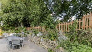 A patio area with a stone wall, a wooden fence, and various plants. - Carreg Winllan (Pen-y-sarn)