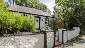 A white house with a black gate, surrounded by greenery and a wooden fence. - Carreg Winllan (Pen-y-sarn)