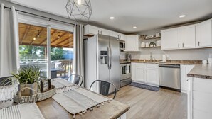 A modern kitchen with white cabinets, stainless steel appliances, and a wooden dining table with a view to the outside.