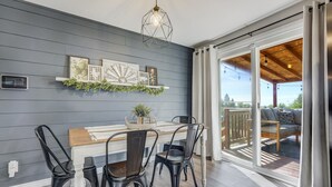 A dining area with a wooden table and black chairs, a decorative wall with framed pictures, and a view of the outdoors through a sliding glass door.