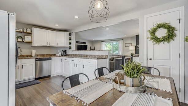 A modern kitchen with white cabinets, a wooden dining table, and a hanging light fixture.