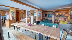 Een ruime woonruimte met een grote houten eettafel, banken, en een gezellige zithoek met een groene bank en een grijze banksofa.