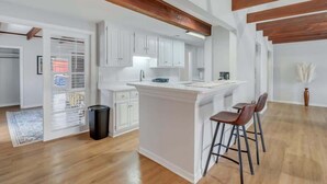 A modern kitchen with white cabinets, a central island, and wooden beams on the ceiling. - Eagle Creek Loft - Close to Shops, Food, GSU! (Statesboro)