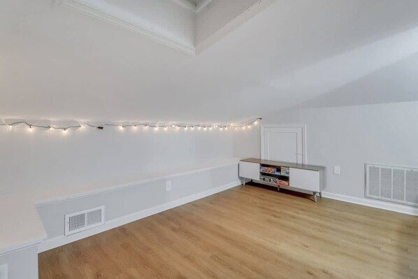 A room with a wooden floor, white walls, a white door, and a small white cabinet with books.