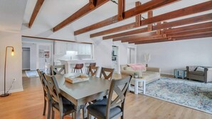 A spacious living area with a wooden dining table, chairs, and a sofa. There is a kitchen in the background with white cabinets and a countertop. - Eagle Creek Loft - Close to Shops, Food, GSU! (Statesboro)