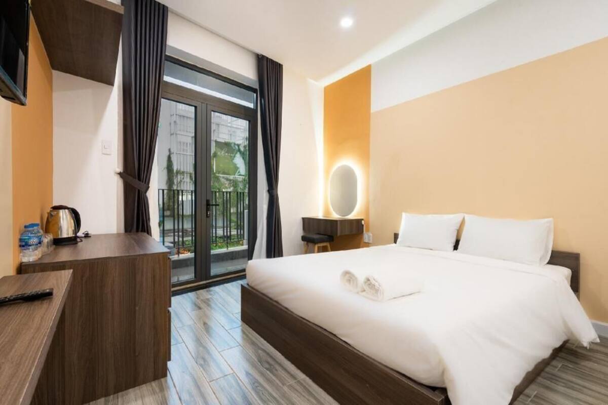 A hotel room with a bed, a desk, a mirror, and a view of the outdoors.