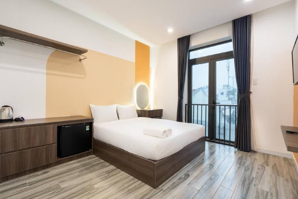 A modern hotel room with a bed, bedside table, and a view through a large window.