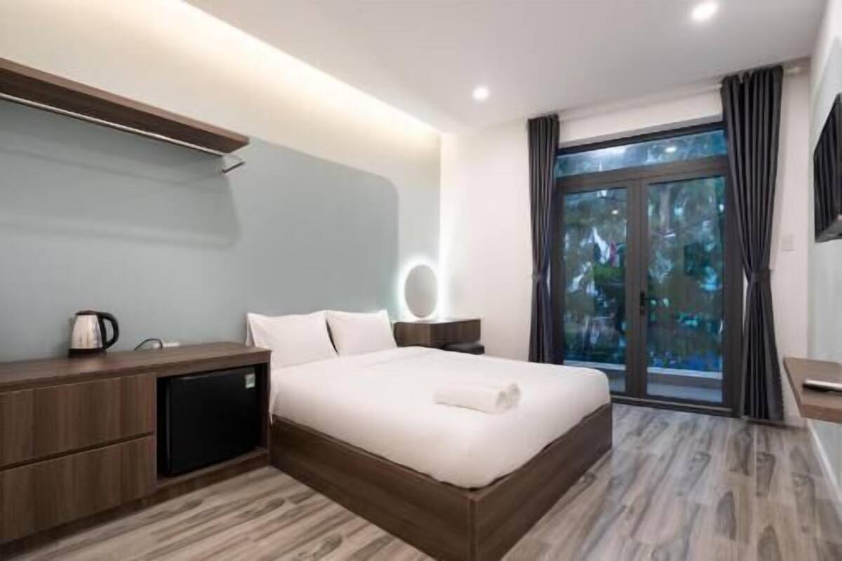 A modern hotel room with a large bed, a bedside table, a mirror, and a window with curtains.