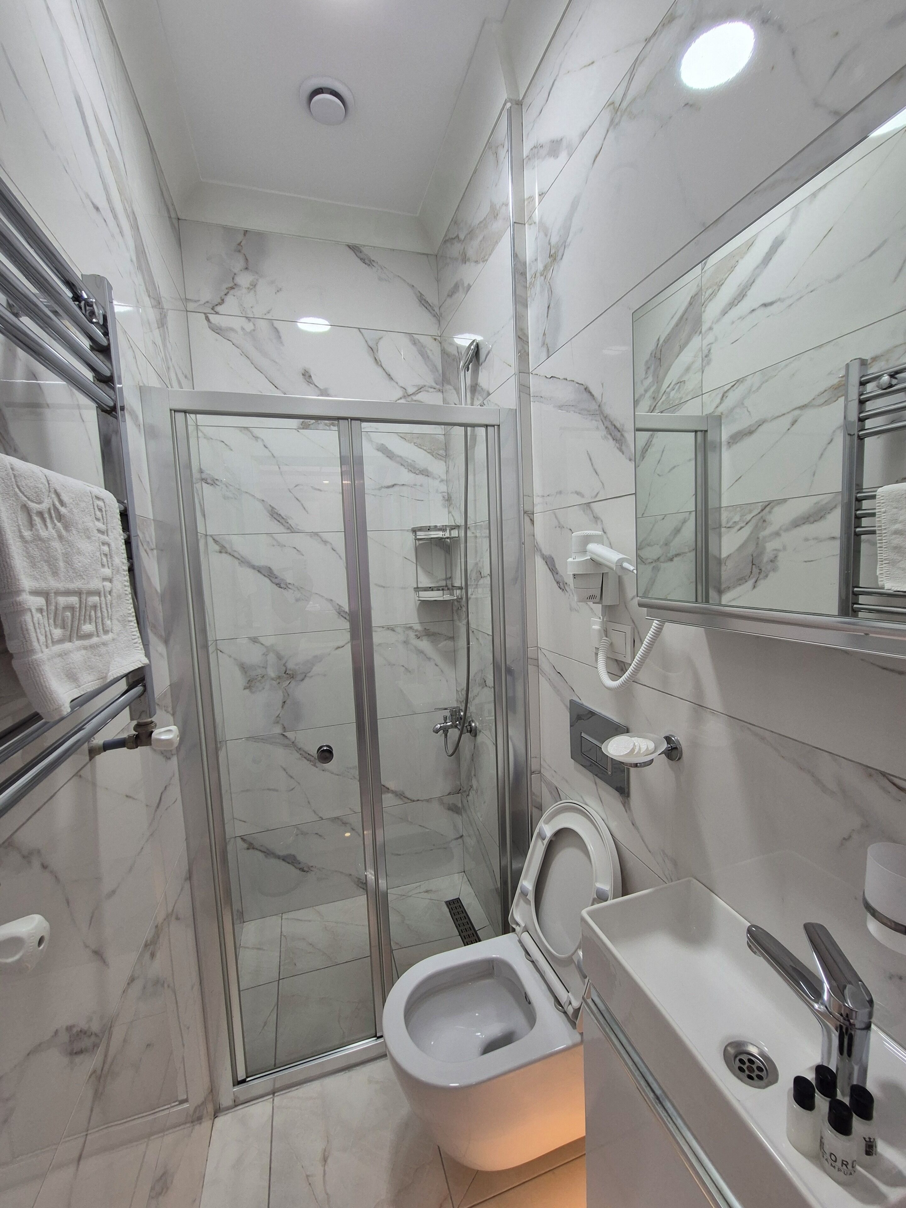 Un baño moderno con ducha envuelta en cristal, inodoro y lavamanos con espejo superior.