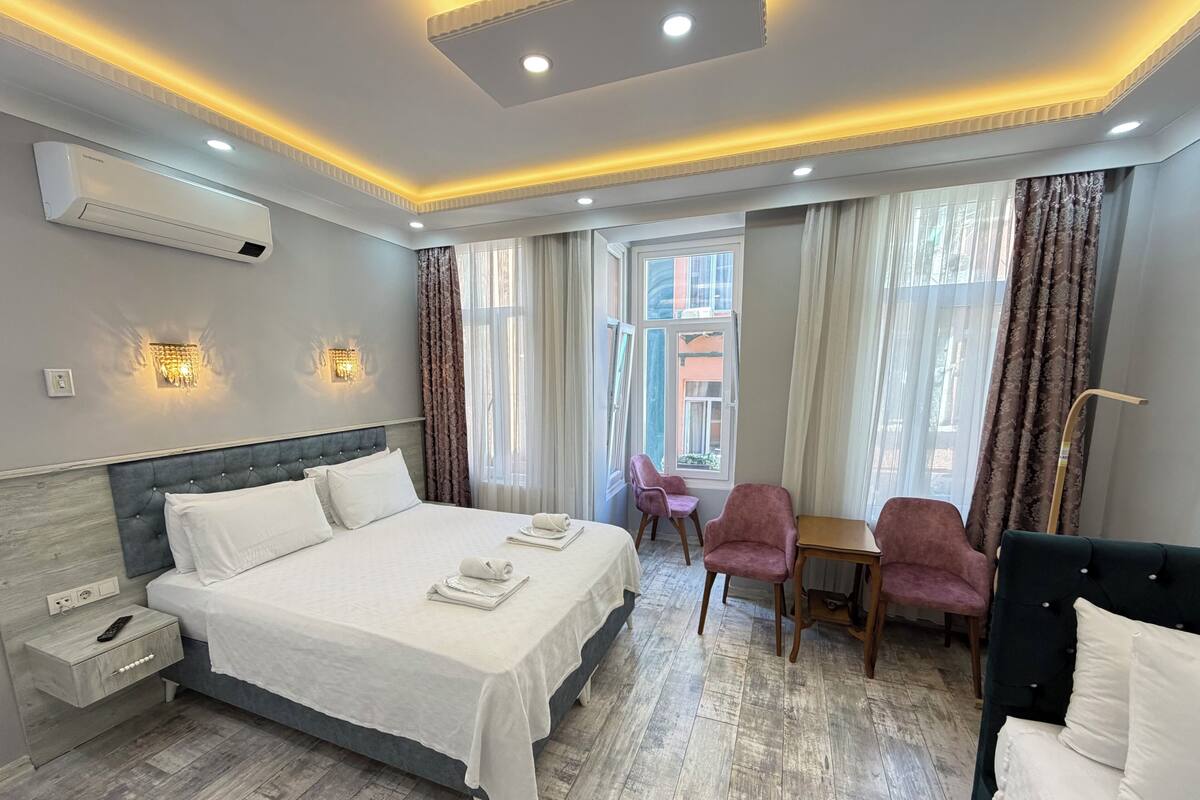 A hotel room with a bed, bedside table, lamp, and a view of the city.
