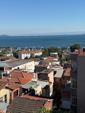 A coastal urban area with buildings, some with red-tiled roofs, and a view of the sea and distant mountains. - Verseca Hotel (Istanbul)
