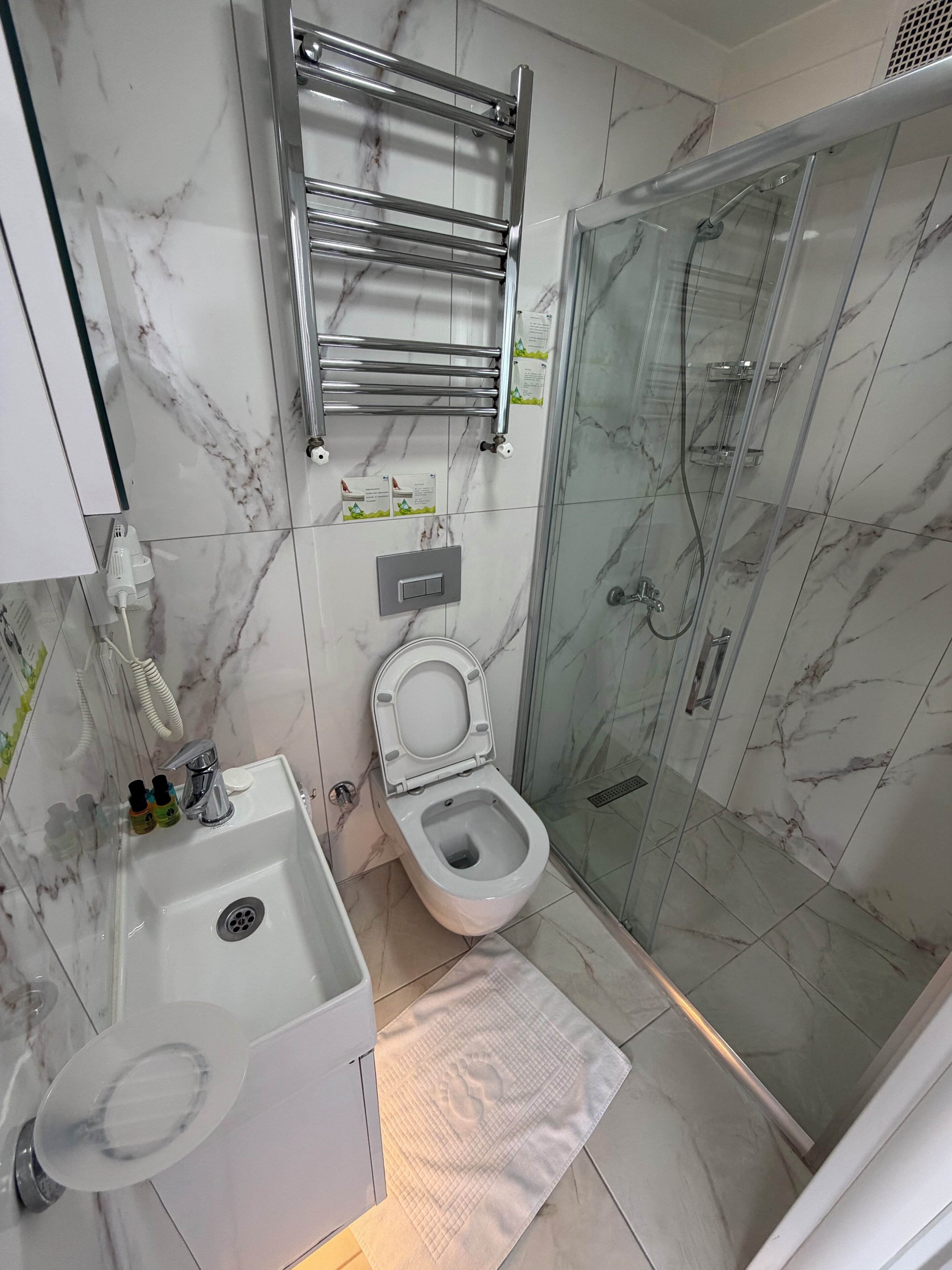 A bathroom with a toilet, sink, glass shower enclosure, and a towel rack.